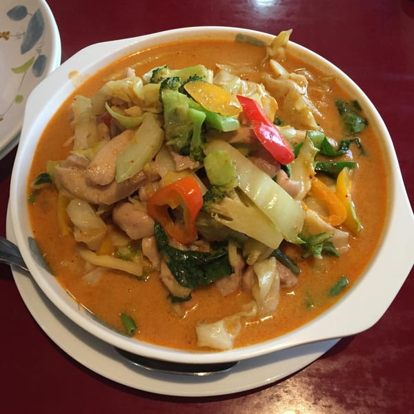 A bowl of Thai red curry with chicken, broccoli, cabbage, and bell peppers on a red table.