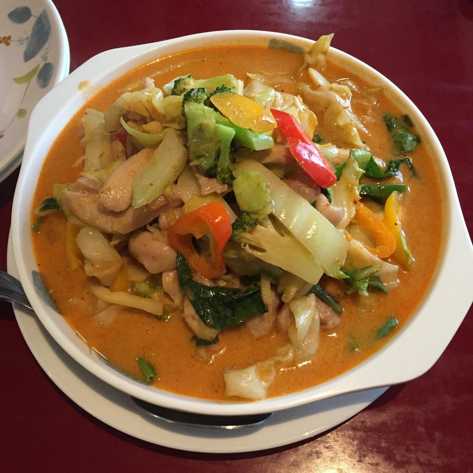 A bowl of Thai red curry with chicken, broccoli, cabbage, and bell peppers on a red table.