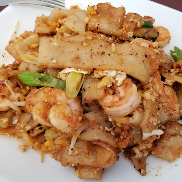 Close-up of Thai Pad See Ew with wide rice noodles, shrimp, egg, and green onions.