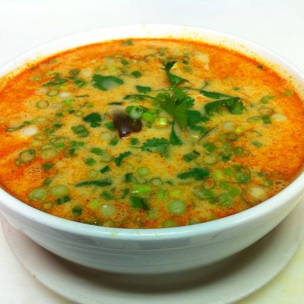 Close-up of a bowl of Thai Tom Yum soup, garnished with green onions and cilantro.