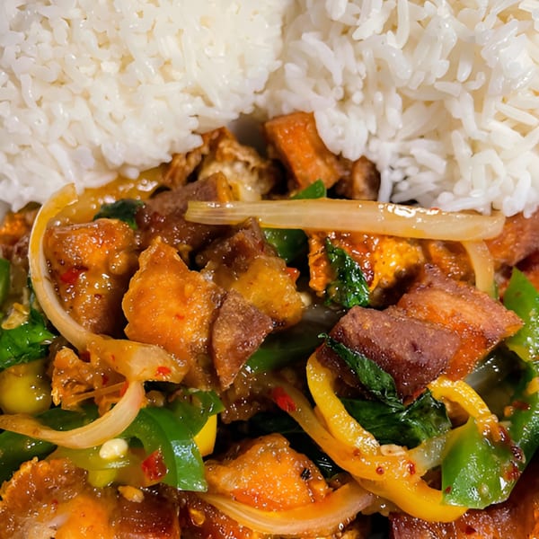 Close-up of Thai crispy pork belly with rice, onions, and bell peppers.
